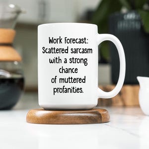 May include: White ceramic coffee mug with a black text design that reads "Work Forecast: Scattered sarcasm with a strong chance of muttered profanities."