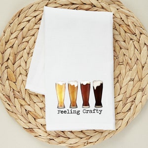 May include: White kitchen towel with a graphic of four beer glasses and the text "Feeling Crafty".