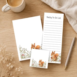 May include: A stationery set featuring a notepad, a square sticky note, and a tall list pad with the text Nutty To-Do List. Each paper item displays a watercolor illustration of a brown squirrel surrounded by green foliage, small flowers, and mushrooms.