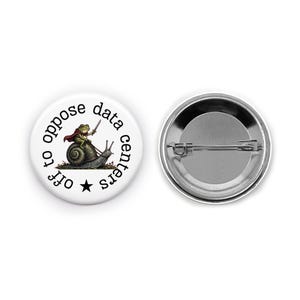 May include: A round pinback button featuring a white background with black text that reads off to oppose data centers and a star. The graphic shows a green frog wearing a red cape and holding a sword while riding a snail. The back is silver metal.