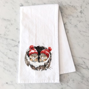 May include: A white kitchen towel with a watercolor illustration of two squirrels wearing red Santa hats in a nest. The squirrels are looking at the viewer.