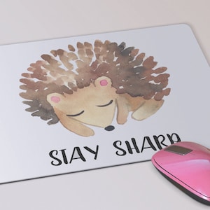 May include: White mouse pad with a watercolor illustration of a brown hedgehog sleeping. The text "STAY SHARP" is printed below the hedgehog.