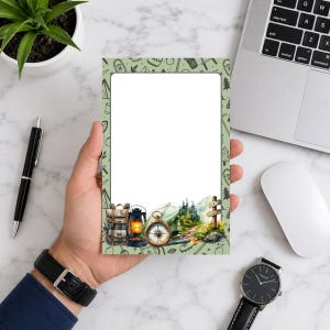 May include: A rectangular notepad with a light green border featuring a repeating pattern of camping icons. The bottom section displays a watercolor illustration of a backpack, a lit lantern, a compass, a tent, trees, and a wooden signpost.