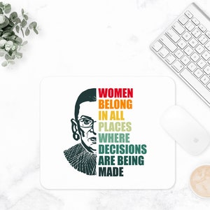 May include: A white mouse pad with a black and white illustration of Ruth Bader Ginsburg. The text "Women Belong In All Places Where Decisions Are Being Made" is written in rainbow colors.