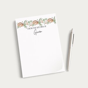 May include: A white notepad with a watercolor illustration of bread and greenery at the top. The text "FROM THE KITCHEN OF Gwen" is printed in black. A silver pen rests beside the notepad.