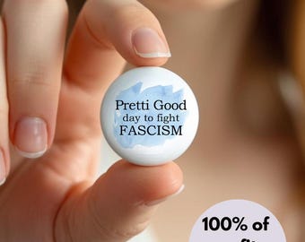 May include: A white button with the text "Pretti Good day to fight FASCISM" in black font, with a blue watercolor design. The button is held in a person's hand. A purple circle with the text "100% of profits donated" is in the lower right.
