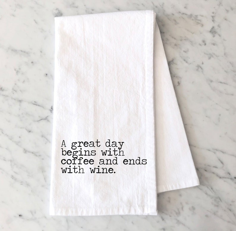 May include: White kitchen towel with black text that reads "A great day begins with coffee and ends with wine."