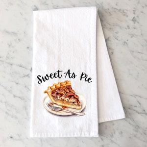 May include: White kitchen towel with a brown and white pecan pie slice on a white plate with a fork. The text "Sweet As Pie" is printed in black cursive font.