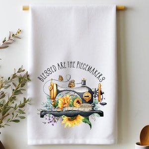 May include: White kitchen towel with a black and gold vintage sewing machine, sunflowers, butterflies, and the text "Blessed are the peacemakers".