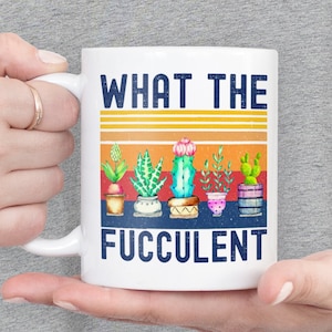 May include: White ceramic mug with a retro-style design featuring the text "WHAT THE FUCCULENT" and a row of potted succulents in various colors.