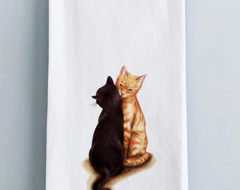 May include: A kitchen towel with a watercolor illustration of two cats. One cat is black and the other is orange. The orange cat is licking the black cat's ear.