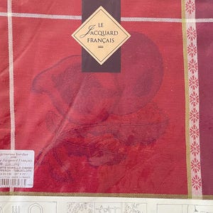 May include: A red and burgundy tablecloth in a plastic package. The tablecloth has a floral design and the words "Le Jacquard Français" on a label. The package also includes illustrations of the tablecloth in use.