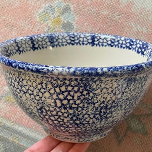 May include: A ceramic mixing bowl with a white interior and a blue patterned exterior. The bowl has a wide rim and a rounded shape. The blue pattern is a repeating design of small, connected shapes. The bowl is held by a hand.
