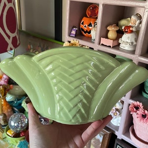 May include: A light green ceramic planter with a woven design. The planter is shaped like a fan and has a wide, flat base.