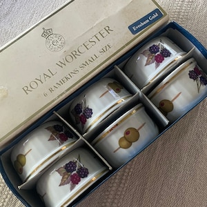 May include: A set of six Royal Worcester ramekins in a box. The white porcelain ramekins feature gold trim and are decorated with either olives on a toothpick or blackberries. The box is labeled "Royal Worcester 6 Ramekins Small Size".