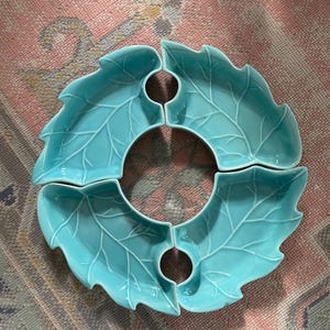 May include: A set of four turquoise leaf-shaped serving dishes. Each dish has a central hole and detailed leaf vein patterns. The dishes are arranged in a circular pattern, suitable for serving snacks or appetizers.