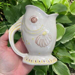 May include: A white ceramic mug with a black handle and the text "But First, Coffee" in a bold, black font. The mug is set against a neutral background, highlighting its simple design.