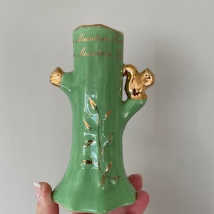 May include: A green ceramic tree trunk vase with gold accents and a squirrel figurine on a branch. The vase has the words "Mountain Brook, Mountain Brook" written on it.