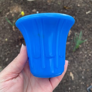 May include: A bright blue glass bud vase with a fluted design. The vase is held in a hand.