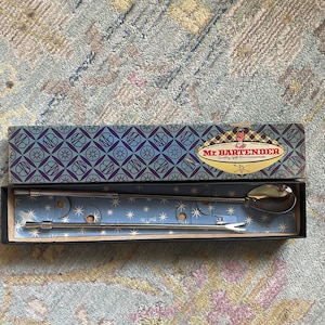 May include: A bar tool set in a box. The box is blue with a repeating pattern and the words "Mr. Bartender" on it. Inside the box are two stainless steel bar tools: a spoon and a fork.