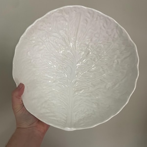 May include: White ceramic bowl shaped like a cabbage leaf. The bowl is large and has a deep, rounded shape.