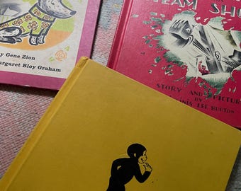 Könnte beinhalten: Eine Sammlung alter Kinderbücher. Ein Buch hat einen rosa Einband mit dem Titel "No Roses for Harry!" und einer Hundeillustration. Ein weiteres Buch hat einen roten Einband mit dem Titel "Mike Mullin and His Steam Shovel". Ein gelbes Buch trägt die Aufschrift "At the Airport".