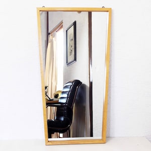 Pode incluir: Um espelho com moldura de madeira e borda chanfrada. O espelho reflete uma sala com uma cadeira de couro preto e uma imagem emoldurada na parede.