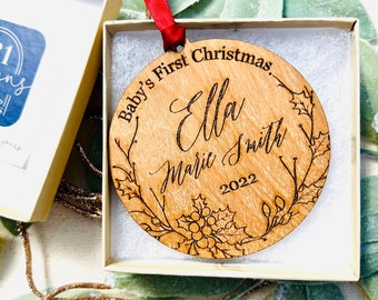 May include: A round wooden ornament with a floral design and the text "Baby's First Christmas Ella Marie Smith 2022".