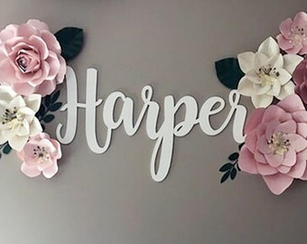 May include: A white wooden sign with the name "Harper" spelled out in cursive letters. The sign is decorated with pink and white paper flowers.