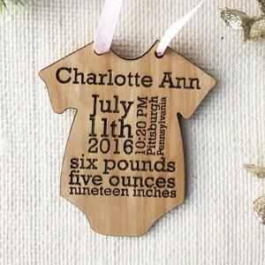 May include: A wooden baby onesie ornament with the text "Charlotte Ann July 11th 2016 10:20 PM Pittsburgh Pennsylvania six pounds five ounces nineteen inches".