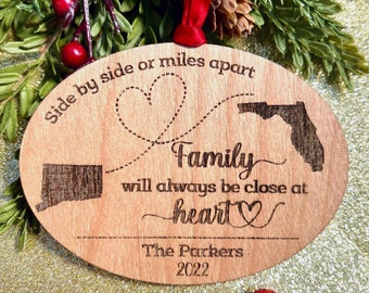 May include: A wooden oval Christmas ornament with a heart design and the text "Side by side or miles apart Family will always be close at heart The Parkers 2022".
