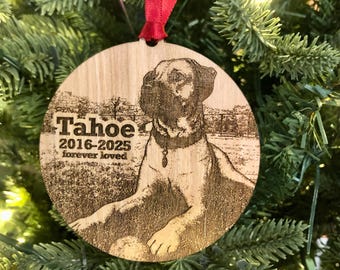 May include: Wooden round Christmas ornament with a laser-etched image of a dog named Tahoe. The ornament includes the years 2016-2025 and the words "forever loved". A red ribbon is attached for hanging on a Christmas tree.