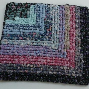 May include: A square braided rug with a geometric pattern in shades of blue, purple, pink, and black.