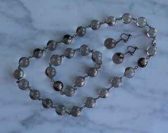 May include: A set of vintage jewelry featuring a necklace, bracelet, and earrings. The jewelry is made of silver and features clear glass beads with a silver foil design.