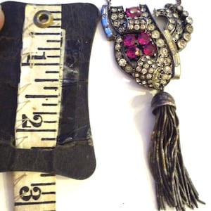 May include: A silver tone necklace with a large pendant featuring a cluster of red and clear rhinestones. The pendant is attached to a tassel.