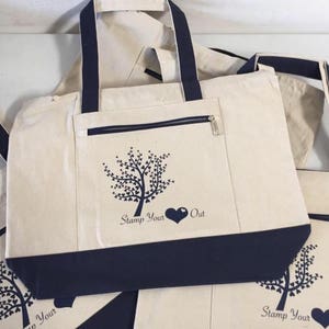 May include: A set of four canvas tote bags with navy blue handles and trim. Each bag features a stylized tree design with a heart and the text "Stamp Your Out".