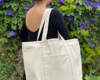 May include: A large, off-white canvas tote bag with a single pocket on the front. The bag has two long straps and is made of a sturdy, natural fabric.