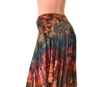 Può includere: Una lunga gonna fluida con un motivo tie-dye in tonalità arancio, marrone, blu e rosa. La gonna è asimmetrica, con un davanti più lungo e un dietro più corto. La gonna è realizzata in un tessuto morbido e confortevole.