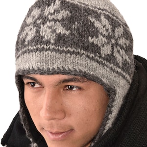 May include: A gray and white knitted wool hat with ear flaps. The hat has a geometric pattern and is worn by a person.