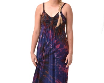 May include: A woman wearing a long, purple, blue, and orange tie-dye maxi dress with thin straps. She is wearing brown sandals.