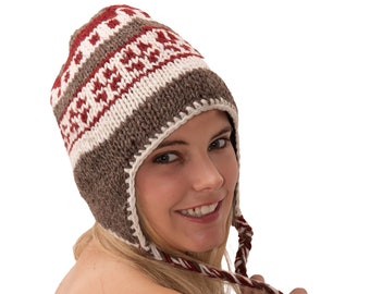 May include: A woman wearing a brown and white knit hat with red accents. The hat has ear flaps that are tied together under her chin.