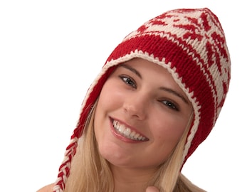May include: A woman with long blonde hair is wearing a red and white knit hat with a long braid hanging down the side of her face. She is smiling and looking at the camera.