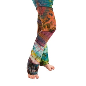 Puede incluir: Leggings teñidos con diseño de retazos. Los leggings presentan una mezcla de azules, verdes, naranjas y morados. La tela parece suave y cómoda, con una abertura acampanada en la pierna. Medidas en centímetros.