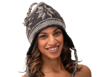 May include: A gray and white knitted hat with a snowflake pattern and long ear flaps. The hat is worn by a person with long brown hair and a strapless top.