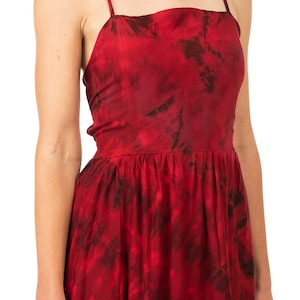 May include: A red tie-dye maxi dress with thin straps. The dress has a fitted bodice and a flowing skirt.