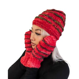 May include: A red knit hat and matching mittens set. The hat and mittens have horizontal stripes of black, green, and yellow. The set is made of a thick, warm yarn, perfect for cold weather.