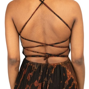 Puede incluir: Un vestido maxi negro con un estampado tie-dye en tonos marrones y naranjas. El vestido tiene una espalda baja con tirantes cruzados.