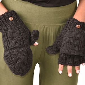 Puede incluir: Un par de guantes sin dedos negros con un patrón de punto de cable y un botón de madera en cada guante.