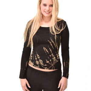 Può includere: Una donna indossa una camicia nera a maniche lunghe con un motivo tie-dye dorato e pantaloni neri.