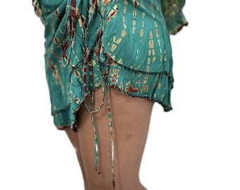 May include: A teal tie-dye sarong skirt with a layered, ruffled hem. The skirt is tied at the waist and features brown and yellow accents. The edges are trimmed with black stitching. The fabric has a flowing, lightweight appearance.